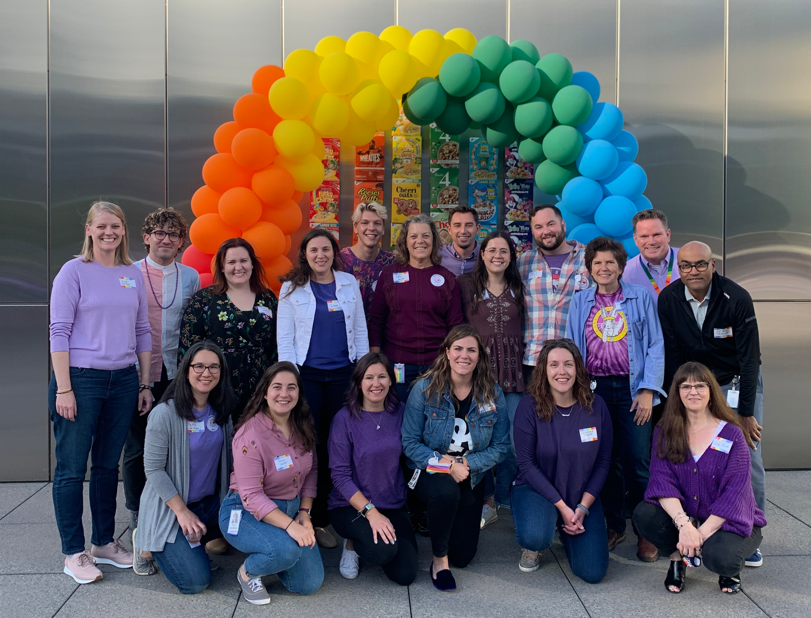 A group of people posing in front of a colorful balloon arch with cereal boxes as the backdrop.